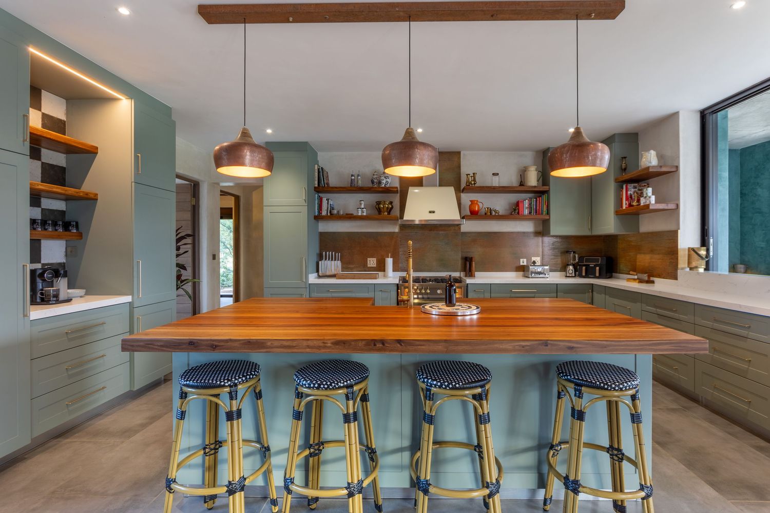 Open-plan kitchen with a timber island, copper pendant lights and sage-green cabinetry